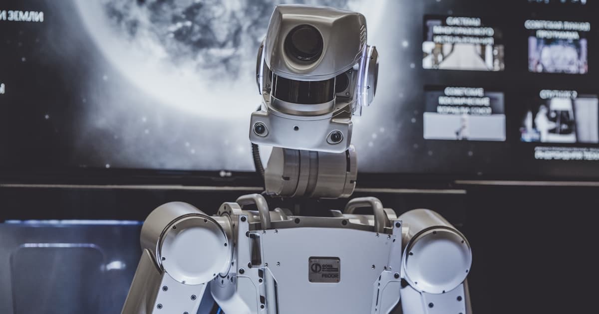 Silver humanoid robot standing in front of a digital display in a technology exhibit