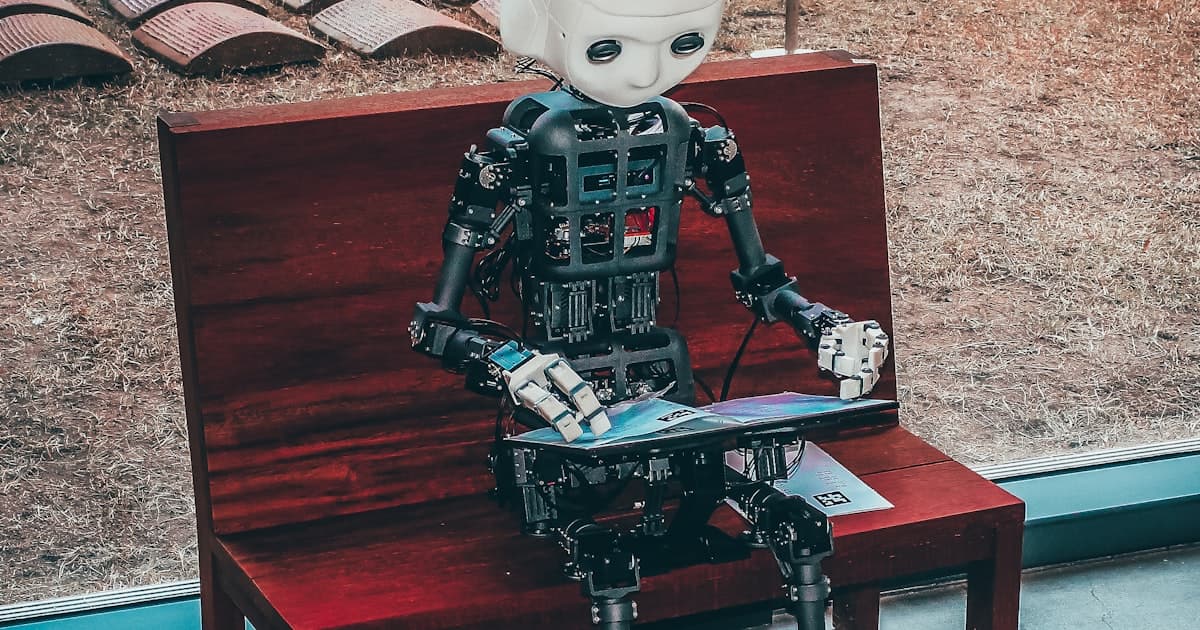 Small humanoid robot sitting on a wooden bench reading a book